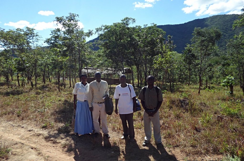 Led by Mr Mhango of Juma (far right) the four stand at the site where the Juma Catholic Community conngreagate for liturgy in the shelter behind them