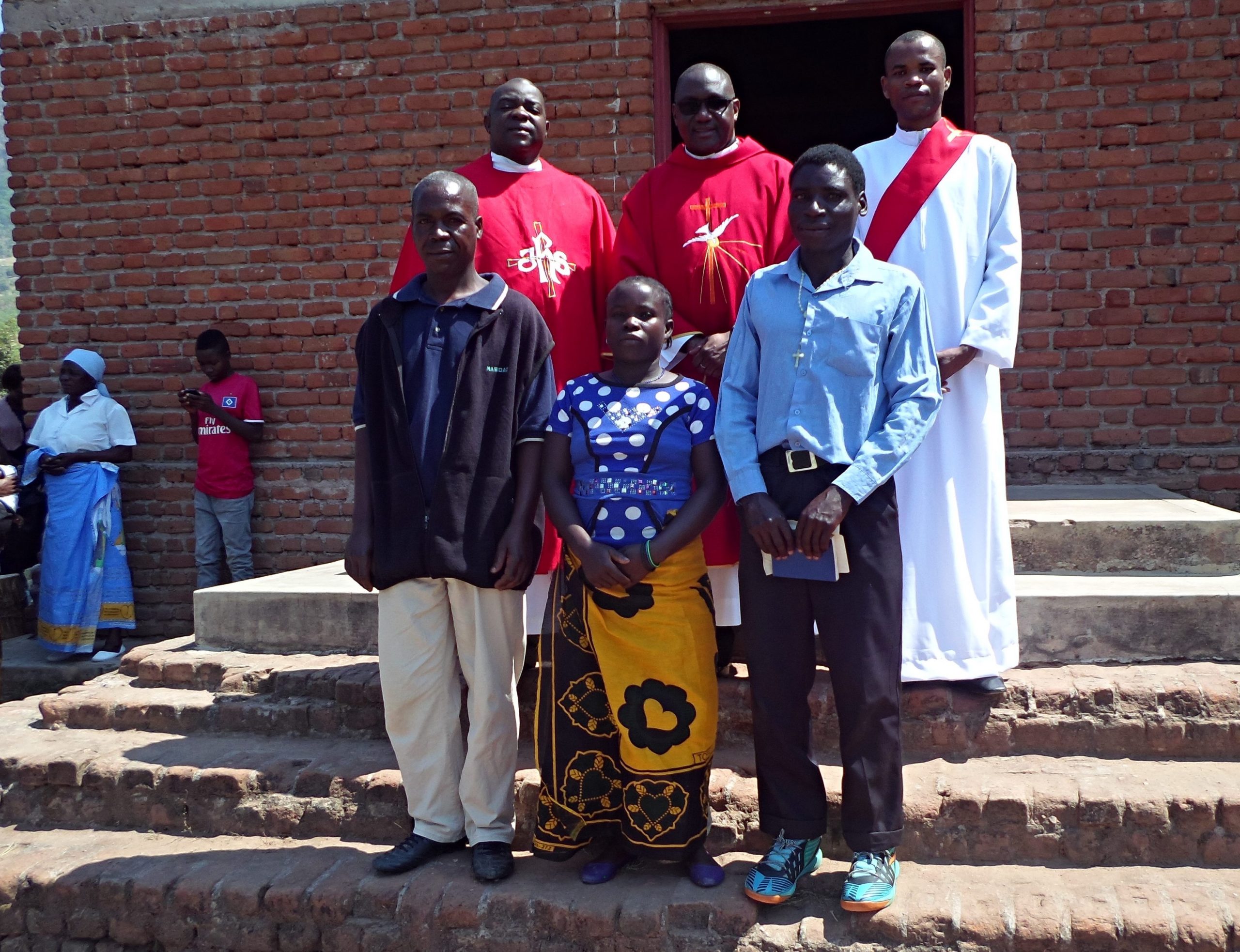 Innocent Harawa (with hymn book in his hands), Nancy Kapira (lady) and Kumbukani Nyirenda (next to Nancy) have a photo with the Vicar General (in specs behind Nancy).