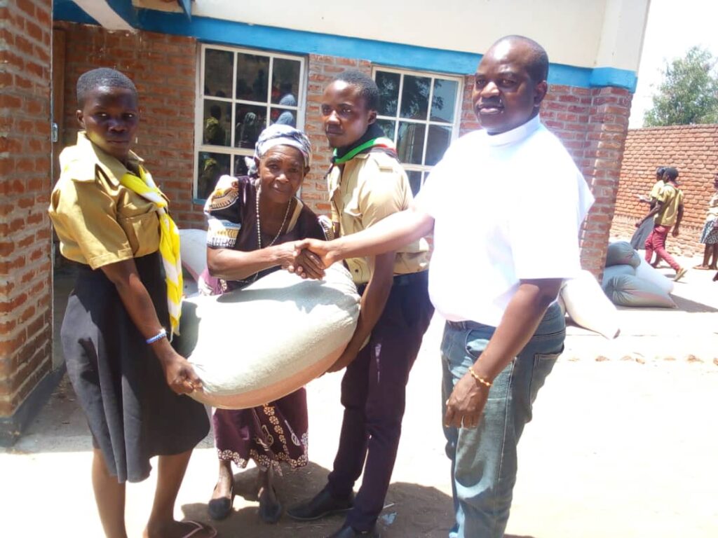 Father Songa shaking hands with a beneficiary who is flanked by Catholic Scouts